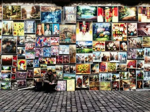 Man selling colorful paintings and artwork on a cobblestone street, ideal for online art or photo selling platforms.