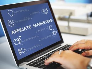 Laptop screen displaying affiliate marketing benefits with icons for reputation, clients, connections, content, traffic, and revenue, hands typing on keyboard.