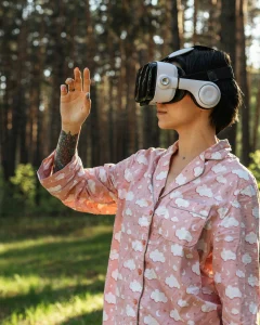Person using a virtual reality headset outdoors in a forest, interacting with the environment while wearing pajamas