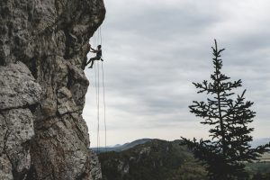 Man rock climbing on steep mountain cliff with safety ropes, symbolizing challenges, risks, and overcoming obstacles.
