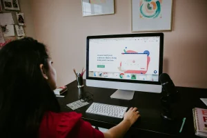 Person working on a computer in a home office, focusing on a screen displaying marketing content with a microphone and desk accessories nearby.