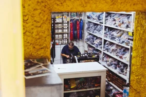 Man working in a small repair shop surrounded by shelves filled with neatly packed products and tools.