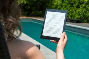 Person reading an eBook on a Kobo tablet while relaxing by a swimming pool on a sunny day