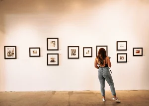 Photographer examining a gallery wall of framed black-and-white photographs in an art exhibition.