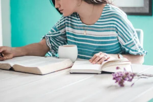 Focused student studying with an open book, taking notes, and enjoying a cup of tea in a cozy learning environment
