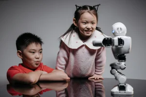 Two children smiling and interacting with a small humanoid robot on a table, exploring AI technology