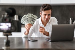 Man recording video with laptop holding cash dollars, showing online income success and digital money making tips.